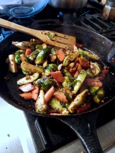 Stir frying the Brussels sprouts, carrot, and fresh ginger in mustard seed and oil.
